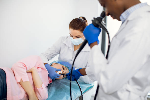 Female young patient lying on the couch in clinic, while male African doctor and Caucasian nurse conducting endoscopy procedure. Focus on patient